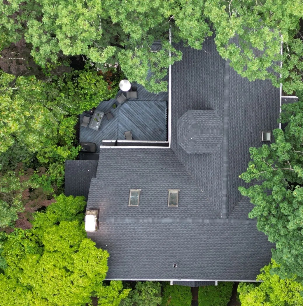 Top-down view of finished asphalt shingle roof with clean roof edges and surrounding trees