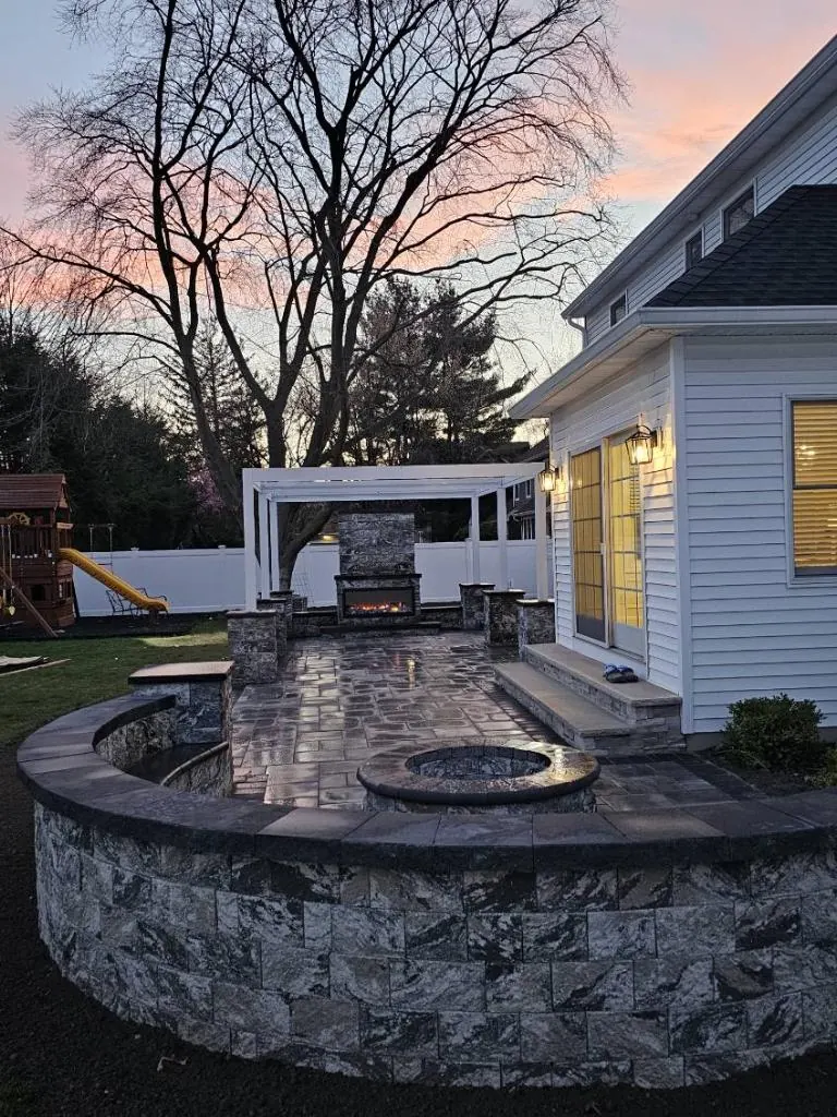 Backyard stone patio with outdoor fireplace, sitting wall, steps, and paver surface